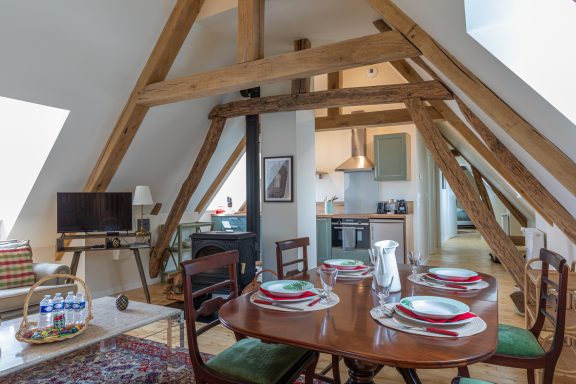 Coin repas chaleureux Gemütlicher Essbereich mit Holztisch, Geschirr und sichtbaren Dachbalken.